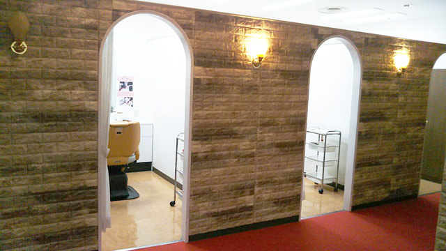 本町国際ビル店の店内廊下の写真。赤絨毯が敷かれ、各室を区切る壁面にはブロック調の装飾が施され、各室の入り口から施術用椅子などが見えている。